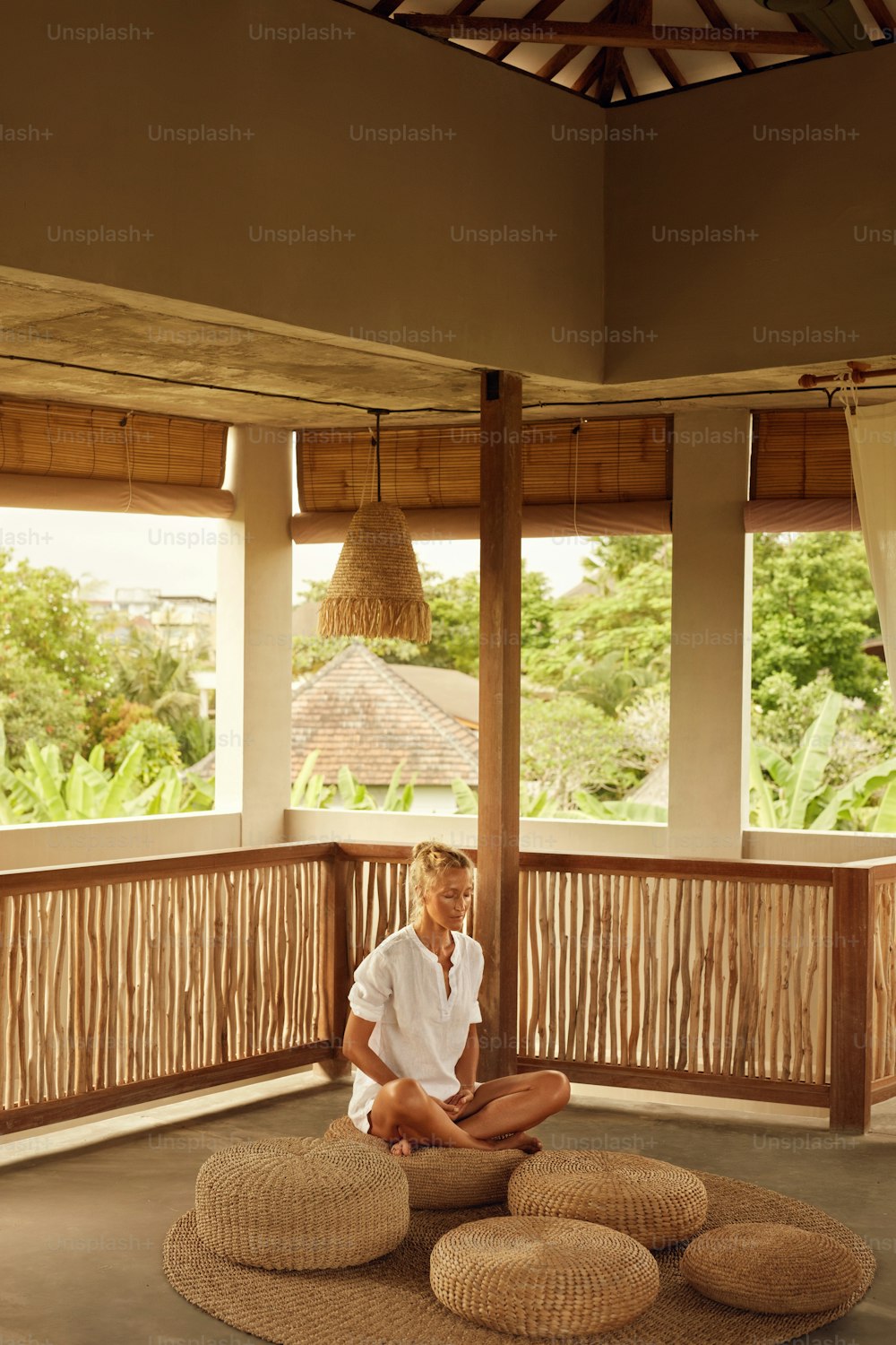 Meditation. Meditieren für Entspannung und mentales Gleichgewicht. Home Yoga Praktizieren für einen gesunden Lebensstil. Reife Frau sitzt auf niedrigem Sitz in Lotuspose auf der Terrasse.