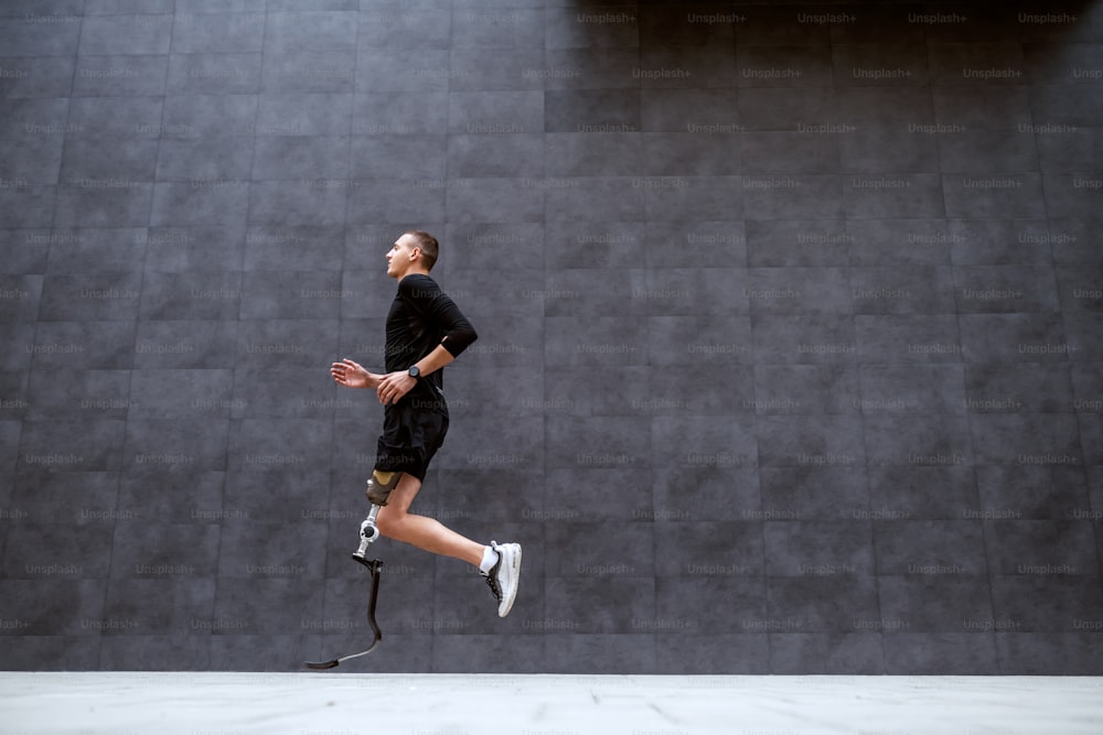 Side view of handsome fit caucasian sportsman with artificial leg running outside.