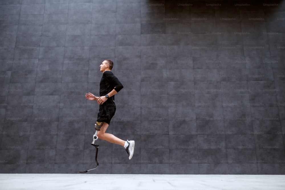 Vista lateral de un guapo deportista caucásico en forma con una pierna artificial corriendo al aire libre.