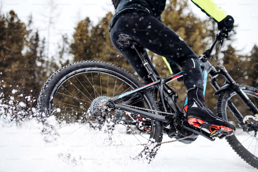 A midsection of mountain biker riding in snow outdoors in winter.