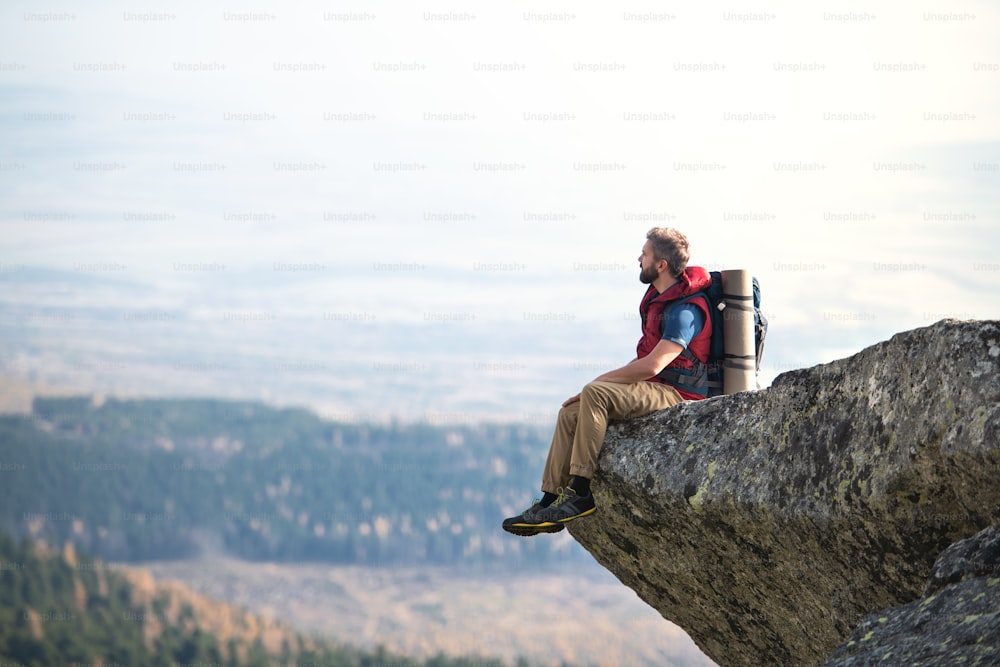 Mature man with backpack hiking in mountains in autumn, resting on rock. Copy space.