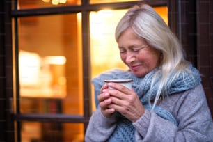 A senior woman with coffee standing outdoors on terrace, resting in the evening.