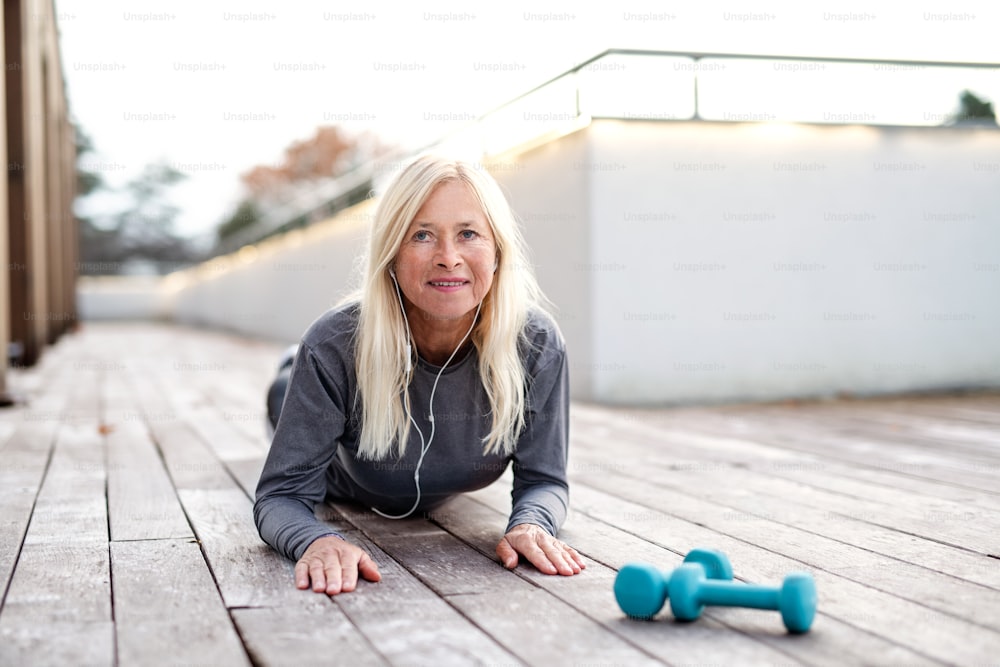 A front view of senior woman doing exercise outdoors, stretching.