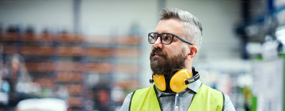 Technician or engineer with protective headphones standing in industrial factory. Copy space.