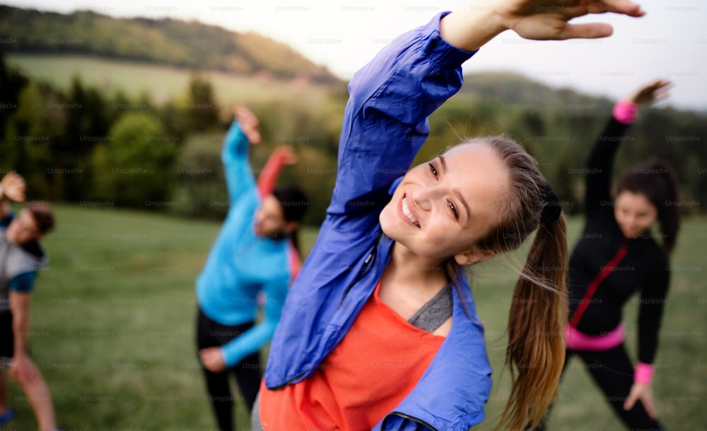 Um grande grupo de pessoas em forma e ativas fazendo exercícios na natureza, alongamento.