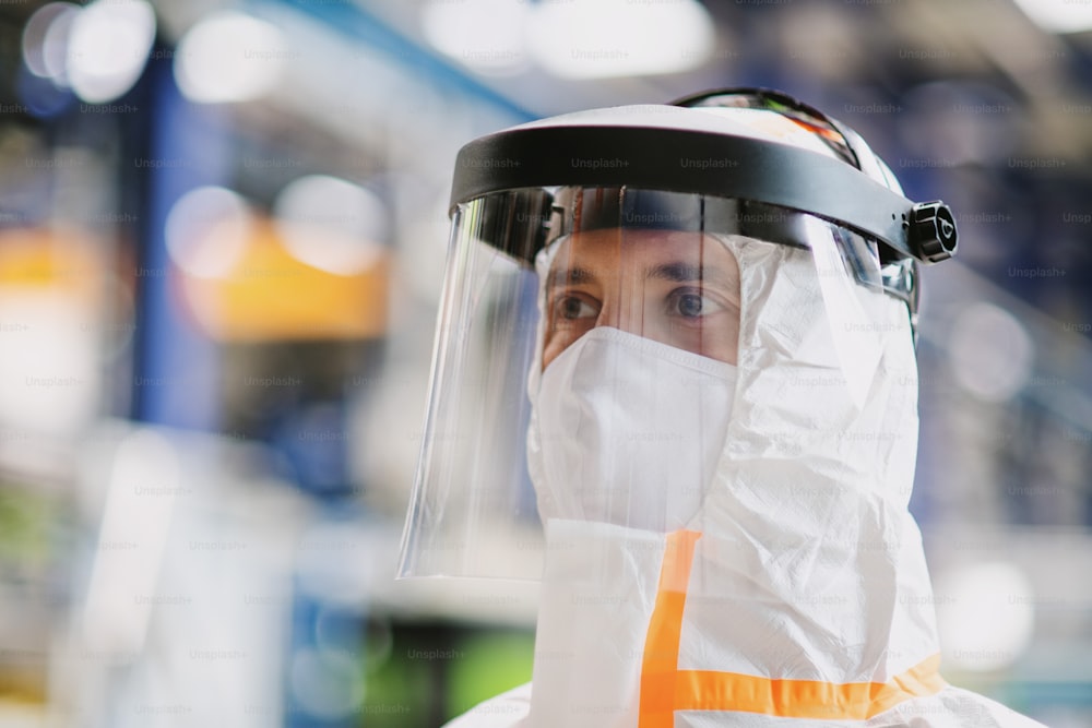 Close-up portrait of worker with protective mask and suit in industrial factory. Copy space.