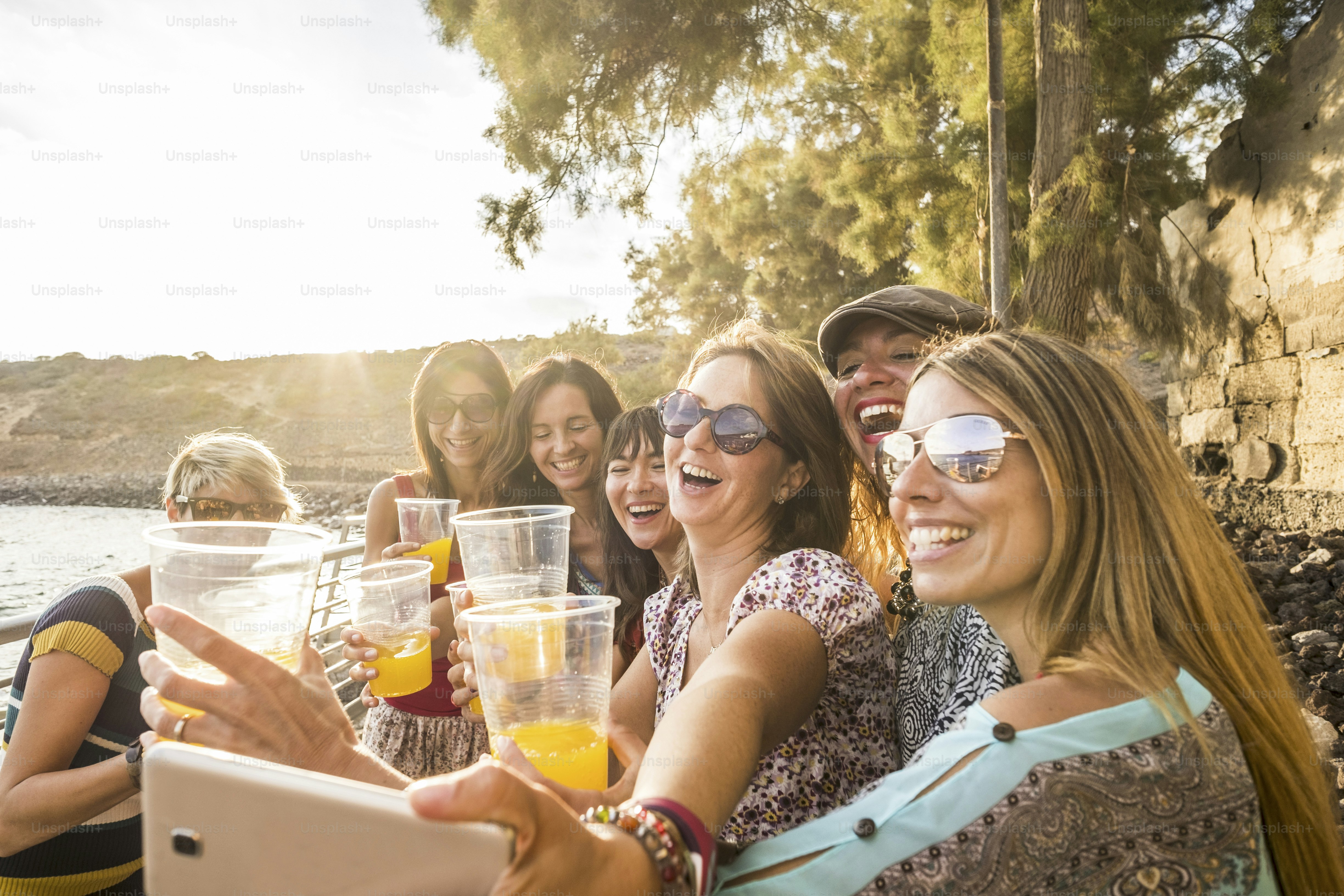 group of young beautiful caucasian woman taking selfie in vacation leisure activity outdoor near the beach and the ocean. sunset time with backlight and lot of smiles and happiness together in friendship forever