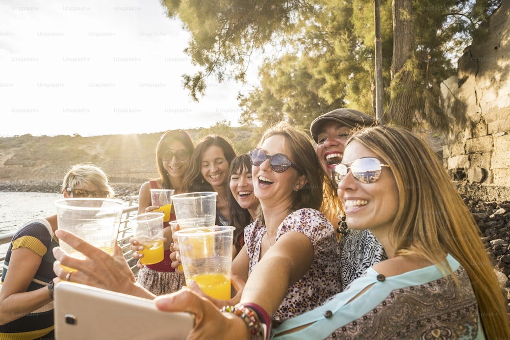 group of young beautiful caucasian woman taking selfie in vacation leisure activity outdoor near the beach and the ocean. sunset time with backlight and lot of smiles and happiness together in friendship forever