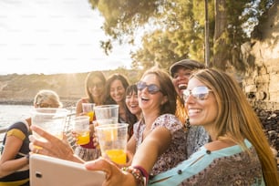 group of young beautiful caucasian woman taking selfie in vacation leisure activity outdoor near the beach and the ocean. sunset time with backlight and lot of smiles and happiness together in friendship forever