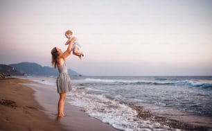 A young mother with a toddler girl on beach on summer holiday, having fun. Copy space.
