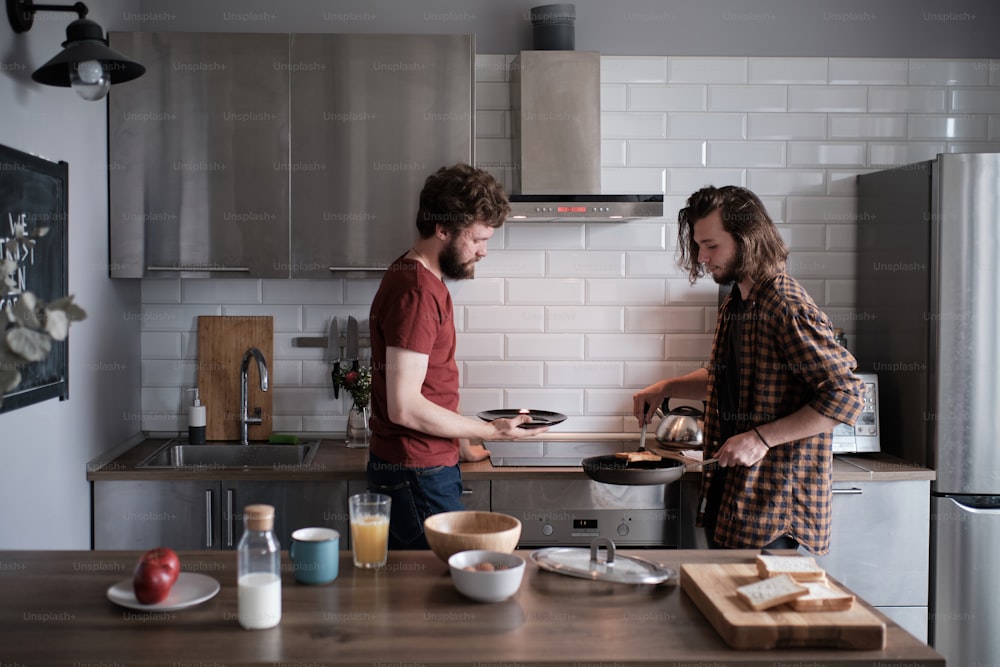 Close up de dois homens fazendo café da manhã juntos na cozinha, um está segurando uma panela, outro está usando espátula
