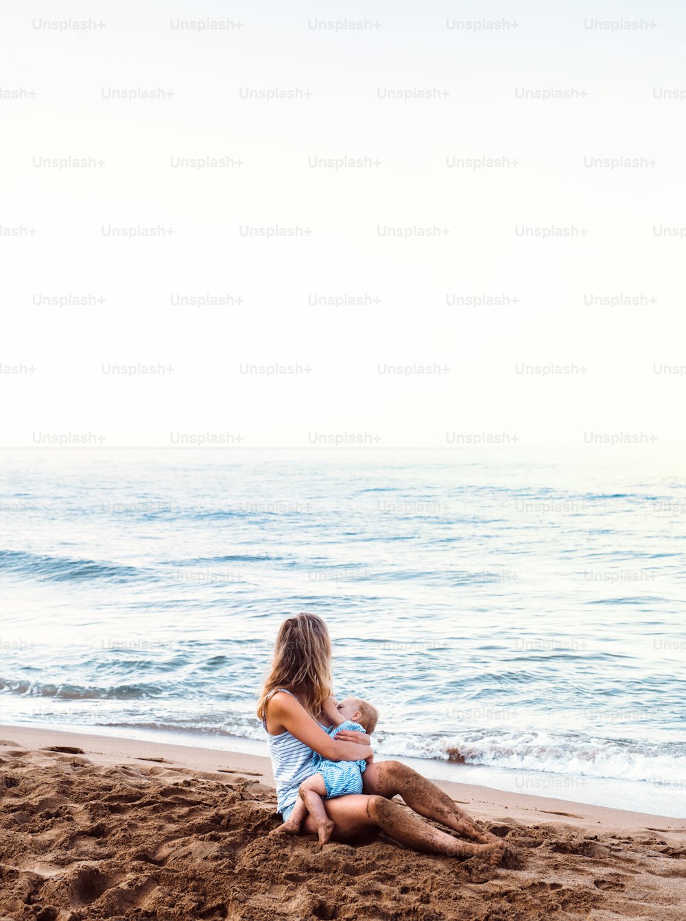 여름 휴가에 해변에서 어린 딸을 먹이는 젊은 어머니.