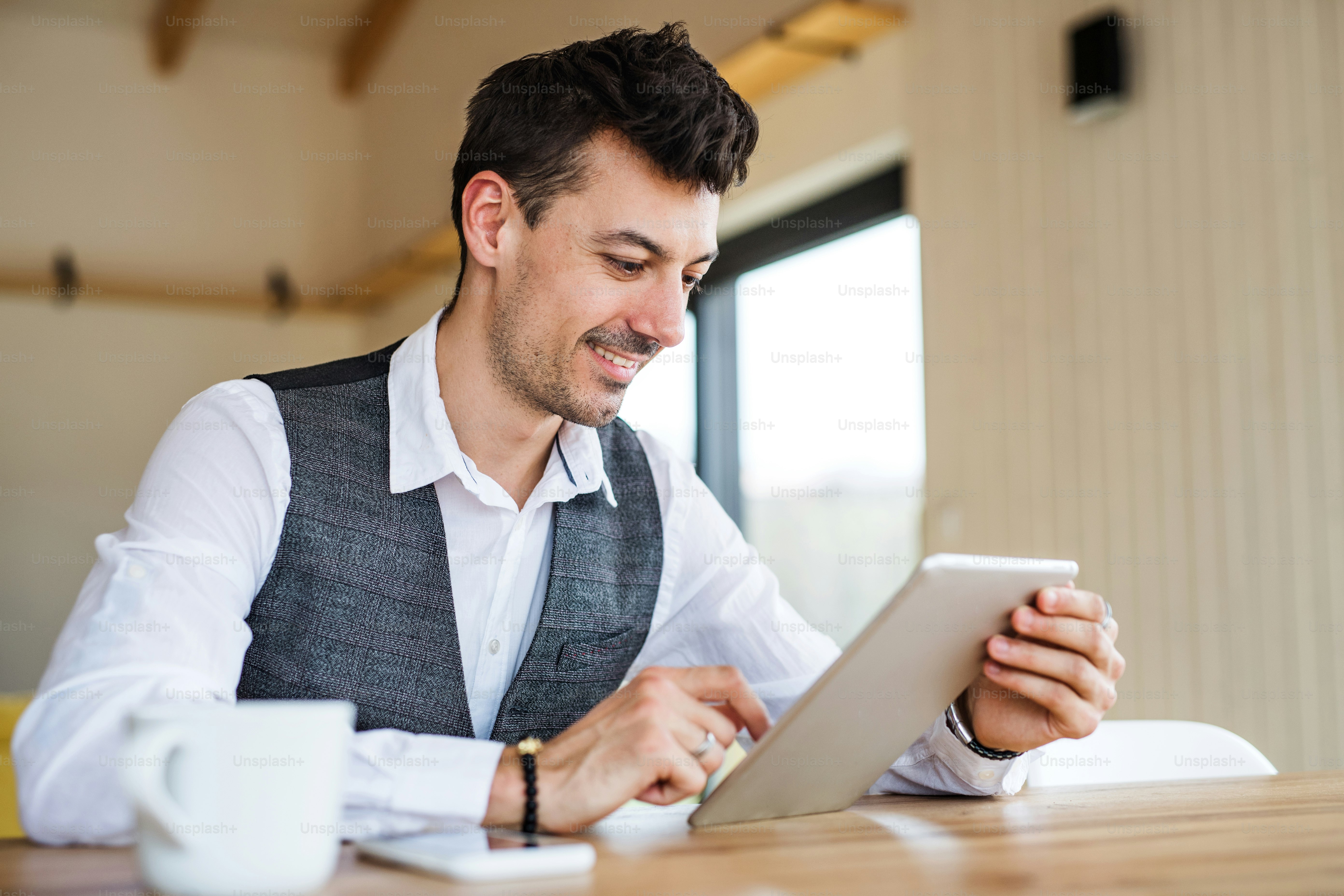Junger gutaussehender Mann mit Kaffee am Tisch sitzend, mit Tablet.