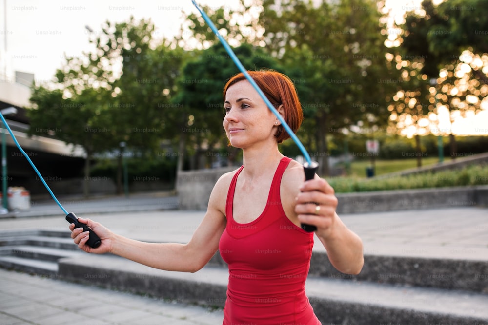 A young woman doing exercise outdoors in city with skipping rope.