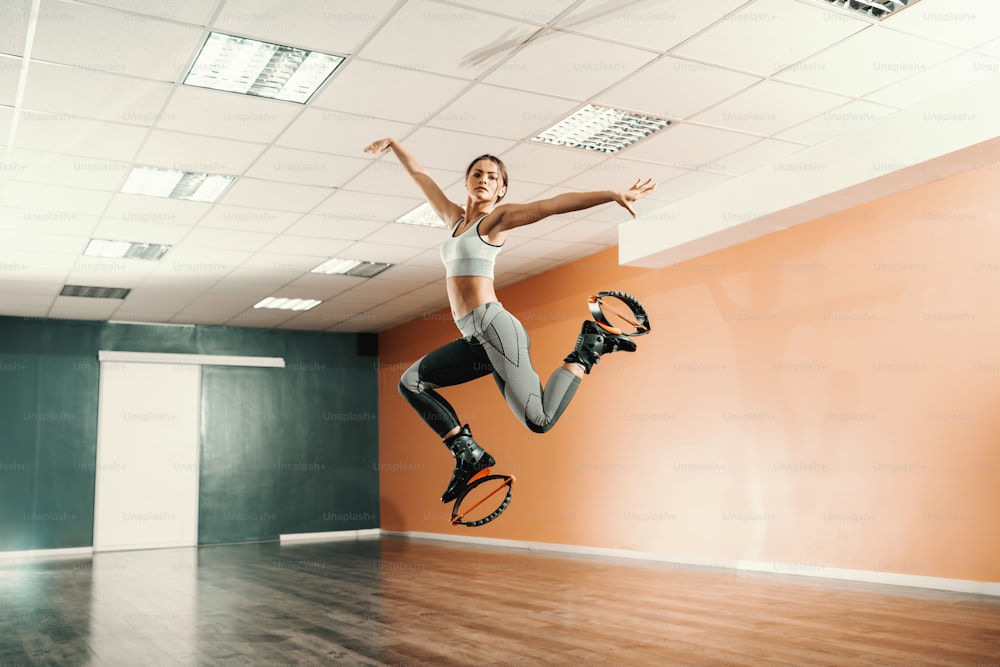 Beautiful fit Caucasian brunette in sportswear jumping on exercise footwear in gym.
