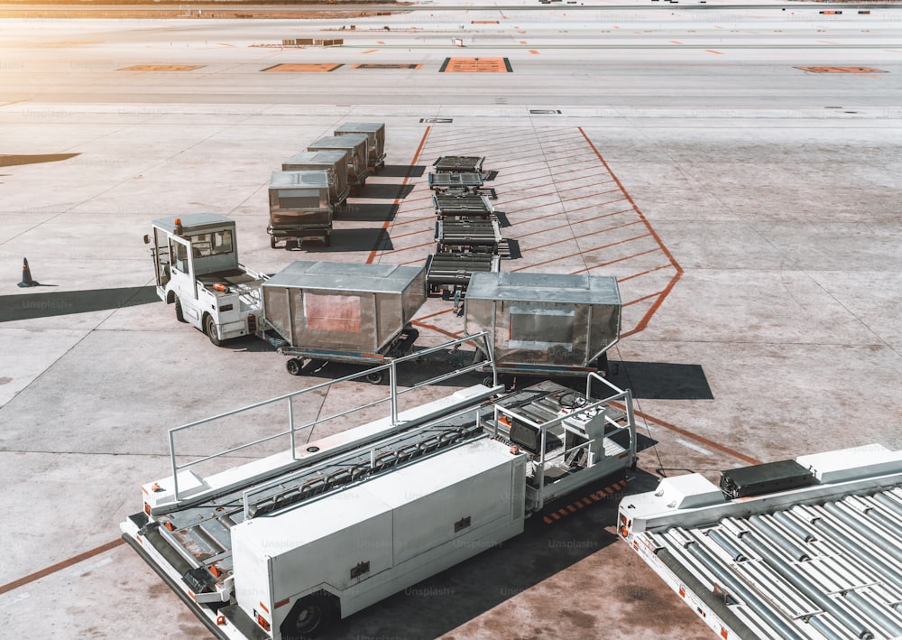 View of machinery on the take-off field with several tractors of different types: one is transporting containers with meal and baggage, second is empty; empty luggage carts; El Part Barcelona Airport