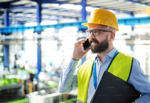 Seitenansicht eines Technikers oder Ingenieurs mit Schutzhelm in einer Industriefabrik mit Telefon.