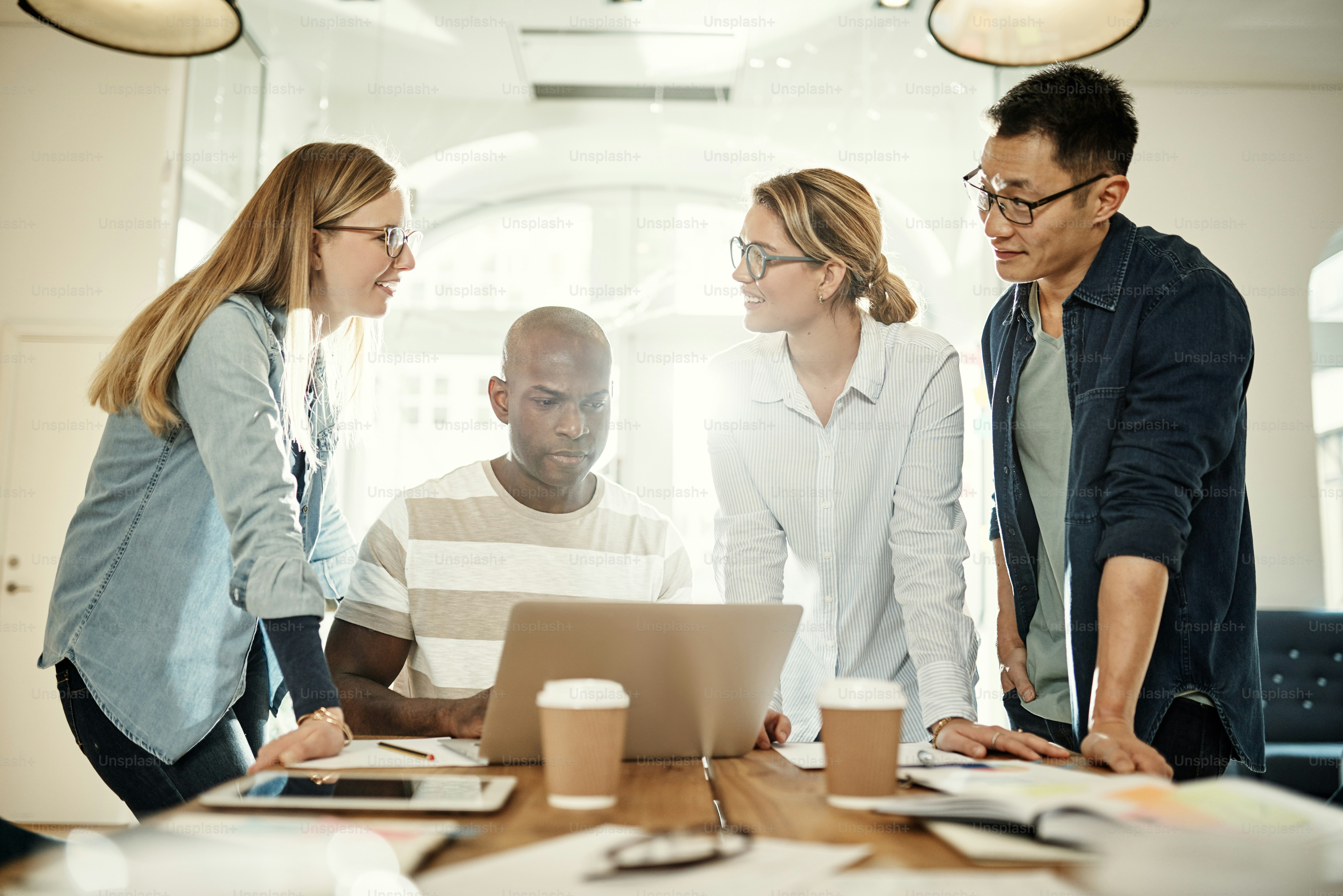 Diverse group of business colleagues talking over a laptop while standing together at a desk in a modern office