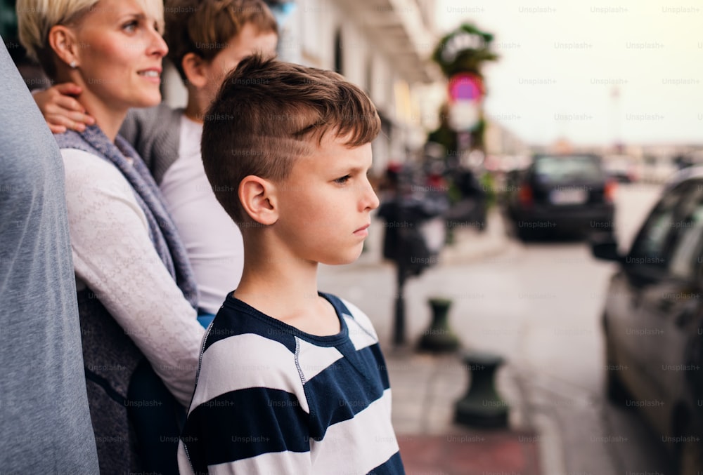 Side view of small boy with family standing outdoors in seaside town.