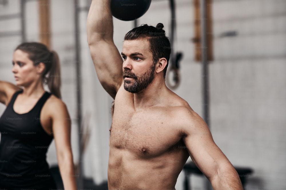 Fit young man lifting a dumbbell over his head during a weightlifting class at the gym