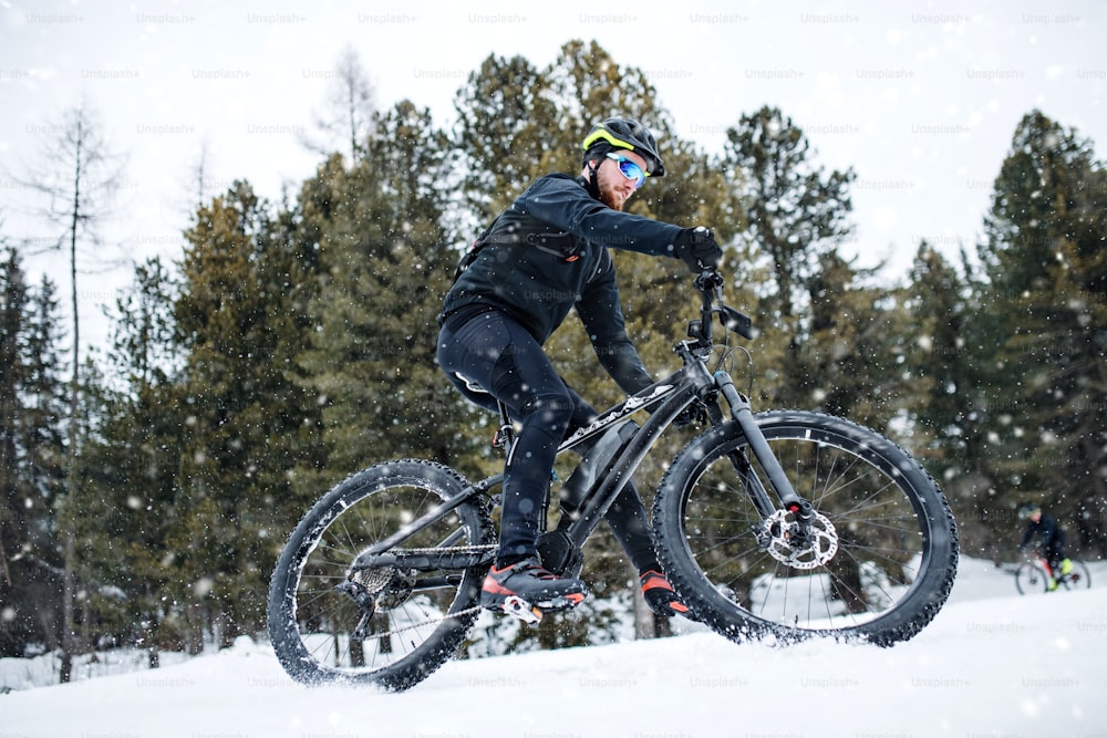 겨울 자연 속에서 야외에서 눈 속에서 산악 자전거를 타는 사람들의 측면 모습.