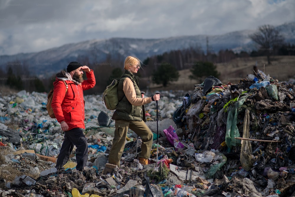Man and woman hikers with walking poles on landfill, environmental and pollution concept.