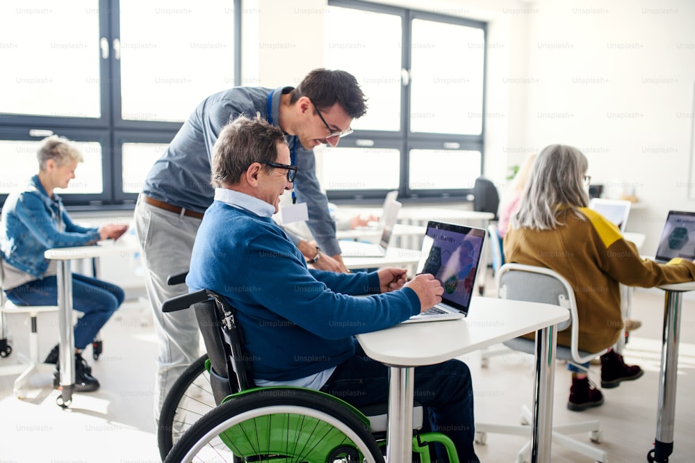 Älterer Mann im Rollstuhl mit Lehrer, der den Computer- und Technologieunterricht besucht.