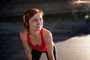 A young woman with headphones resting after doing exercise outdoors in city.