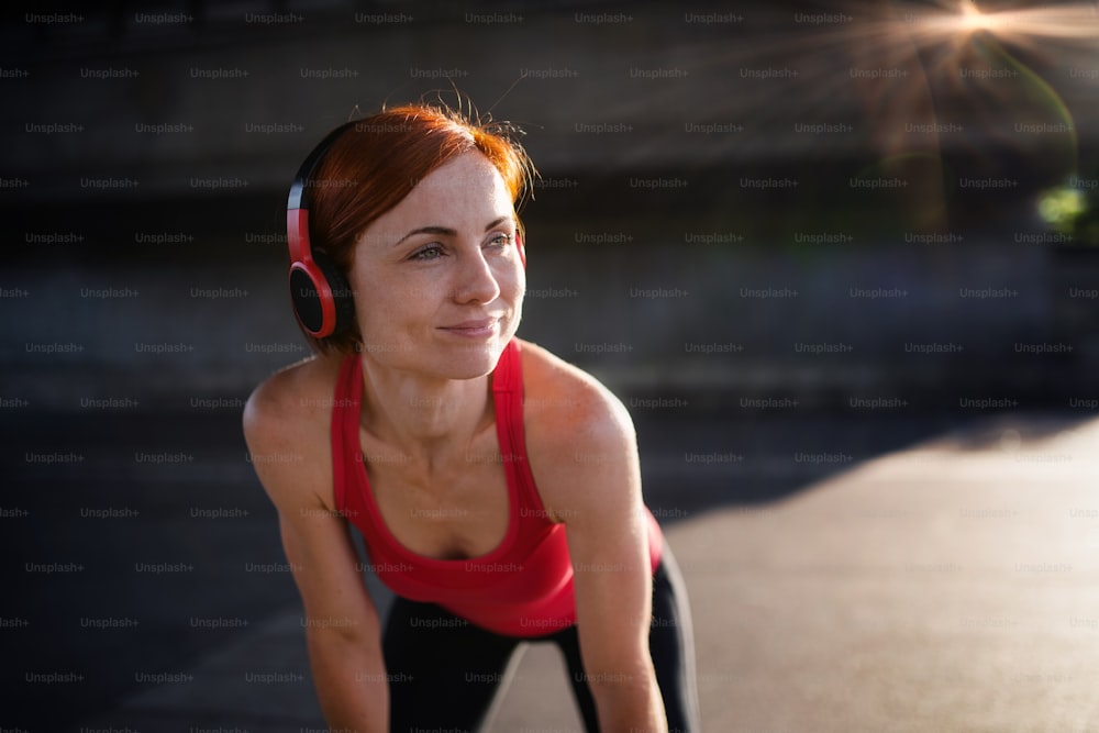 A young woman with headphones resting after doing exercise outdoors in city.