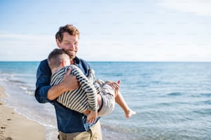 Father carrying small son on a walk outdoors on beach, having fun. Copy space.
