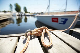 Rope tied in knot in iron loop on wooden surface of pontoon or pier under summer sun
