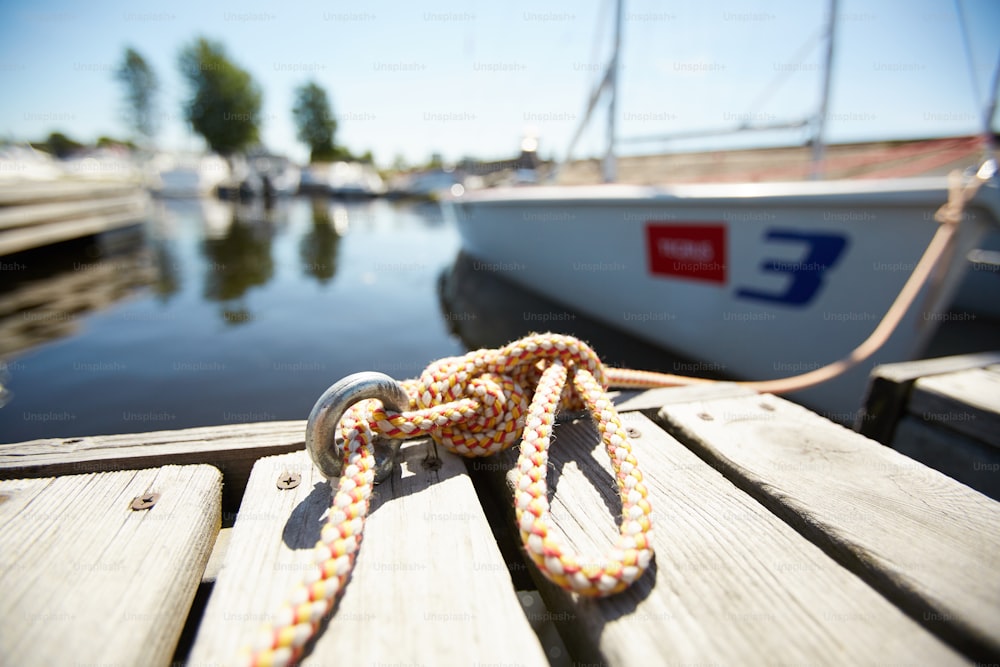 Rope tied in knot in iron loop on wooden surface of pontoon or pier under summer sun