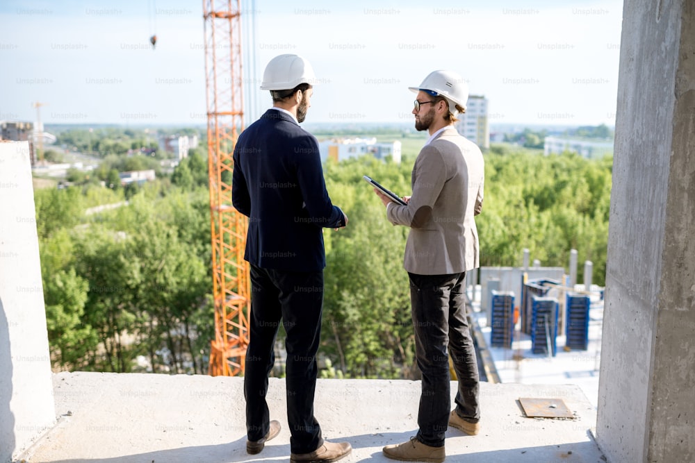 Two engineers or architects supervising the process of residential building construction standing on the structure outdoors