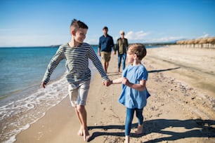 Jeune famille avec deux jeunes enfants marchant pieds nus à l’extérieur sur la plage, s’amusant.