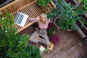 Top view of senior woman with laptop conmputer sitting outdoors on terrace, resting.