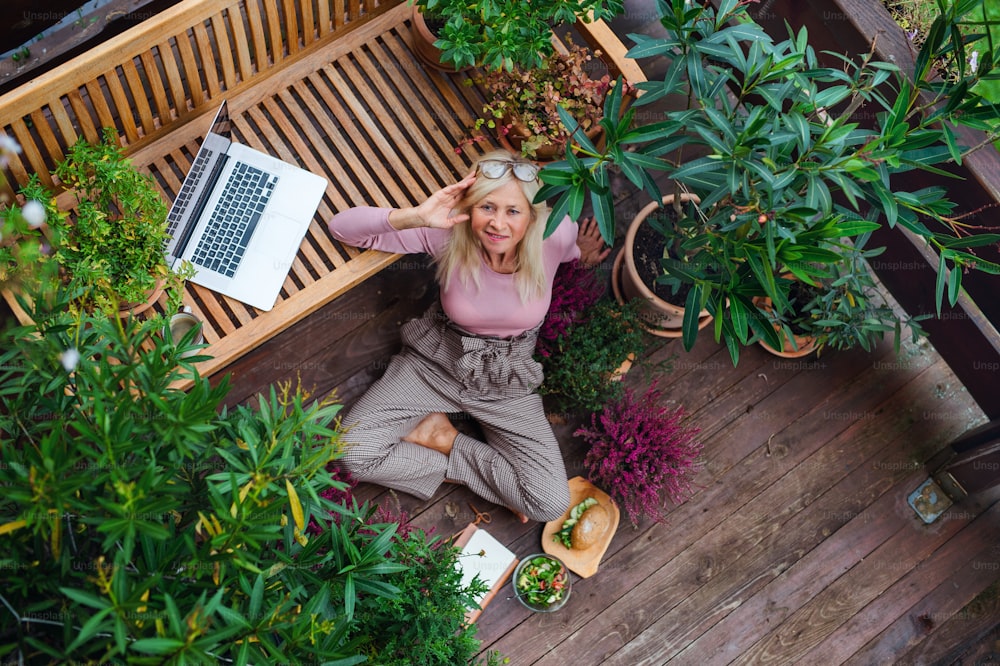 Vista superior de una mujer mayor con ordenador portátil sentado al aire libre en la terraza, descansando.