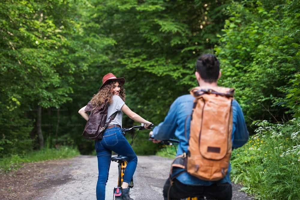 Rear view of young tourist couple travellers with backpacks and electric scooters in nature.