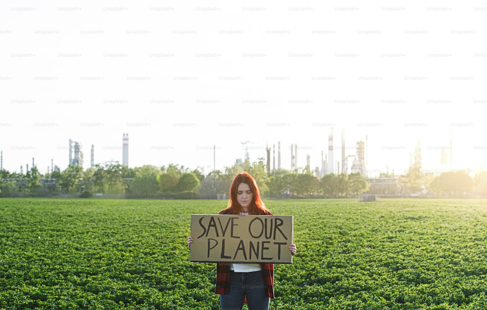 Retrato de una joven activista con un cartel de pie al aire libre junto a la refinería de petróleo, protestando.