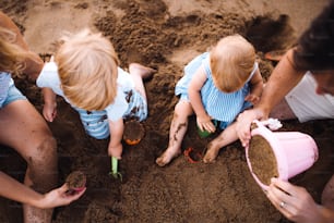 A young family with toddler children playing with sand on beach on summer holiday, a top view and midsection.