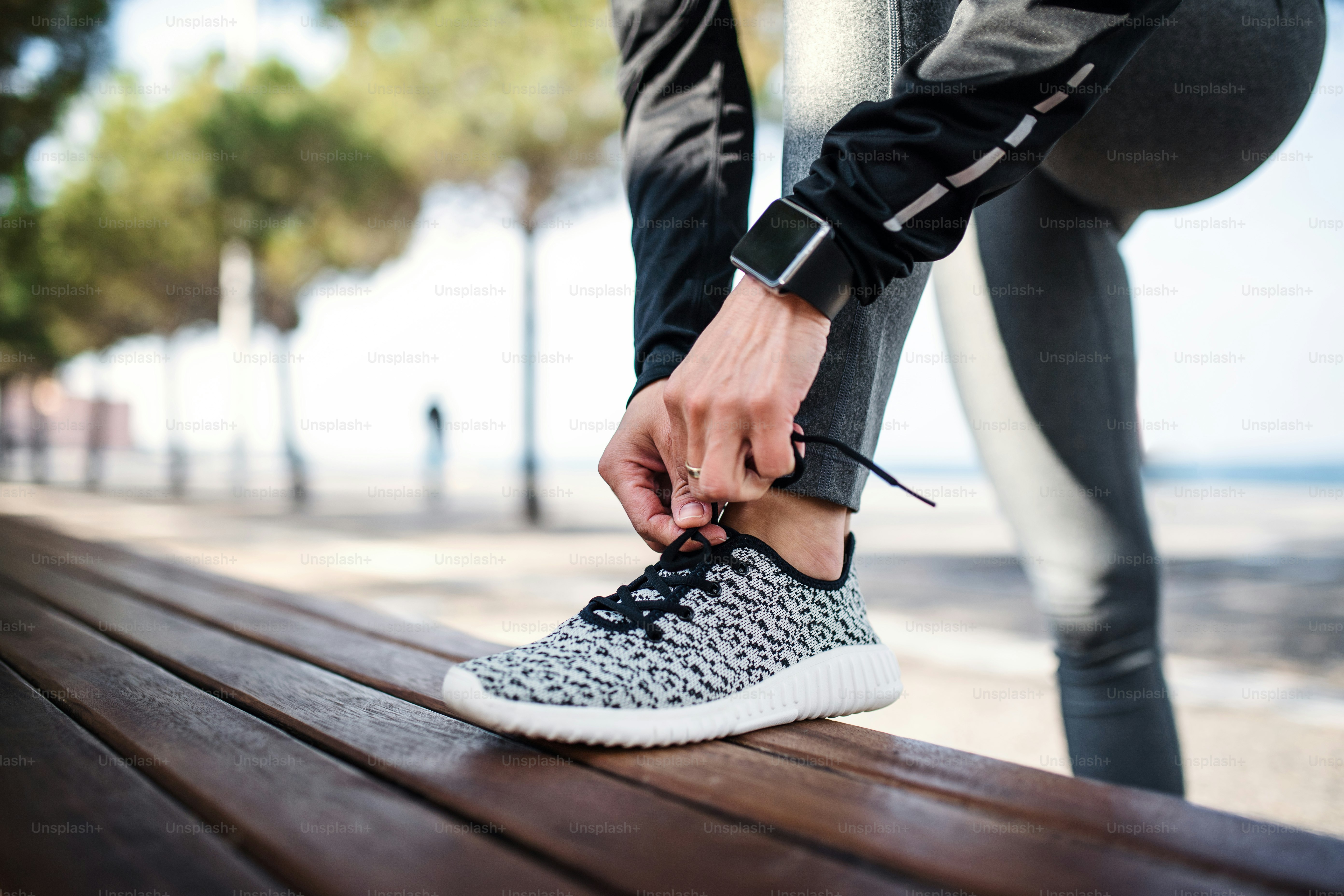 Une section médiane d’une jeune sportive avec une montre connectée à l’extérieur en ville, nouant des lacets