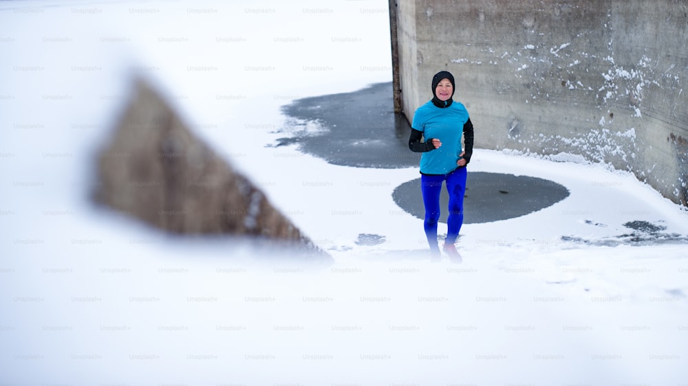 Vorderansicht einer aktiven älteren Frau, die im Winter im Freien läuft und Sport treibt.