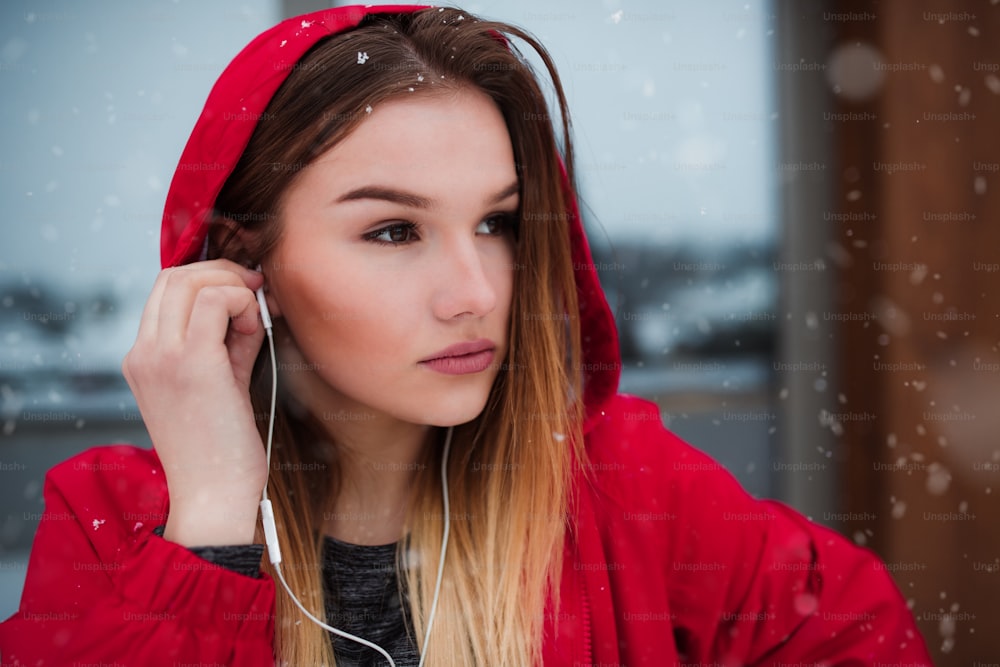 A close-up portrait of beautiful young girl or woman with earphones outdoors, listening to music.