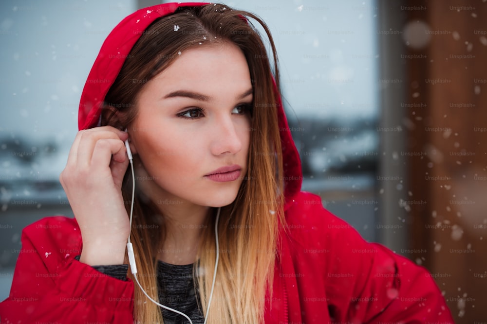 Un retrato de primer plano de una hermosa joven o mujer con auriculares al aire libre, escuchando música.