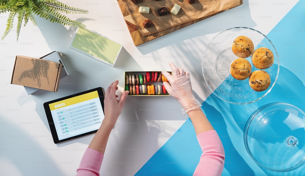 A top view of unrecognizable woman packing biscuits, processing orders desktop concept.