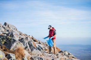 Excursionista maduro del hombre que recoge la basura en la naturaleza en las montañas, concepto de plogging.