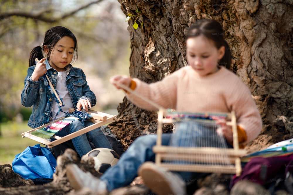 都市公園の屋外に座って手織り機を持った小さな子供たちの肖像画、グループ教育の概念を学びます。