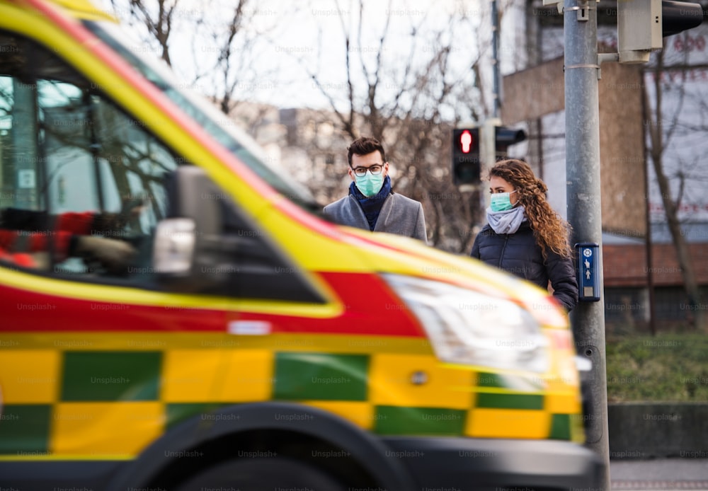 Persone con maschere per il viso in piedi all'aperto in città in ambulanza, concetto di coronavirus.