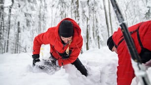 Mountain rescue service on operation outdoors in winter in forest, digging snow with shovels. Avalanche concept.