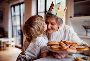Happy senior great grandmother with small toddler boy making cakes at home, kissing.