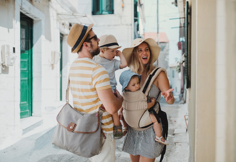 Una familia joven con dos niños pequeños y sombreros caminando por la ciudad en vacaciones de verano.